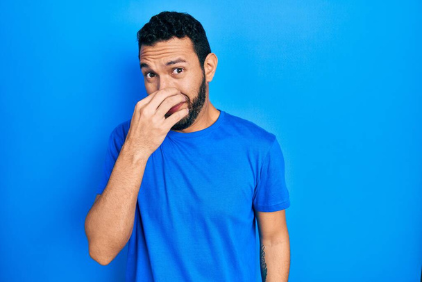 Latinomies, jolla on parta päällään rento sininen t-paita, haisee jotain inhottavaa, sietämätöntä hajua, pidätellen hengitystä sormet nenällä. paha haju  - Valokuva, kuva