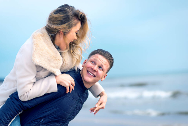Счастливый человек, катающийся на спине к своей женщине и смеющийся над пляжем. Счастливая здоровая пара на свежем воздухе, наслаждаясь жизнью. - Фото, изображение