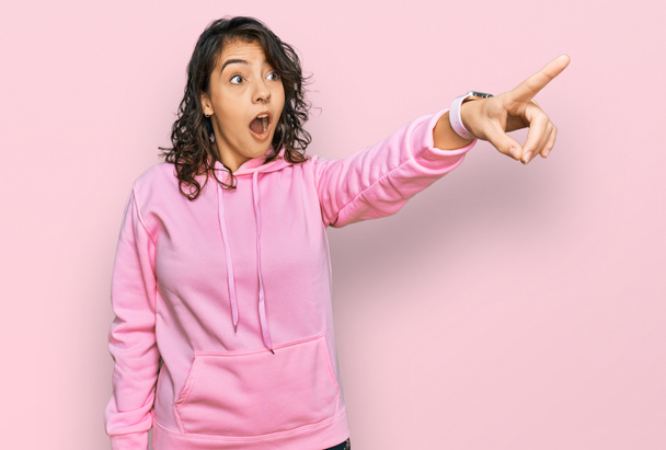 Молода іспаномовна жінка в повсякденному светрі, вказуючи пальцем, здивована попереду, відкритий рот здивований вираз, щось на передньому плані
  - Фото, зображення