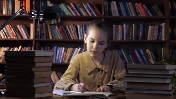 Keskittynyt tyttö takissa kirjoittaa kotitehtäviä muistikirjaan - Materiaali, video