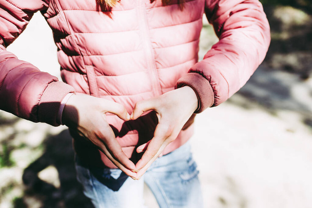 Hands in heart shape. Teenage girl hands heart shape on against forest path background of summer or spring.Closeup - Fotografie, Obrázek