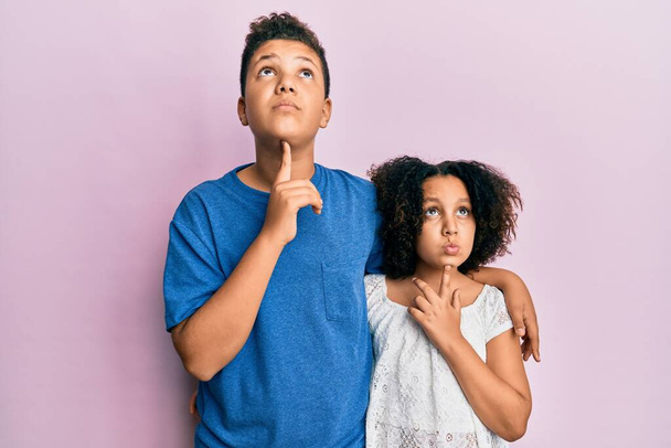 Young hispanic family of brother and sister wearing casual clothes together thinking concentrated about doubt with finger on chin and looking up wondering  - Foto, Imagen