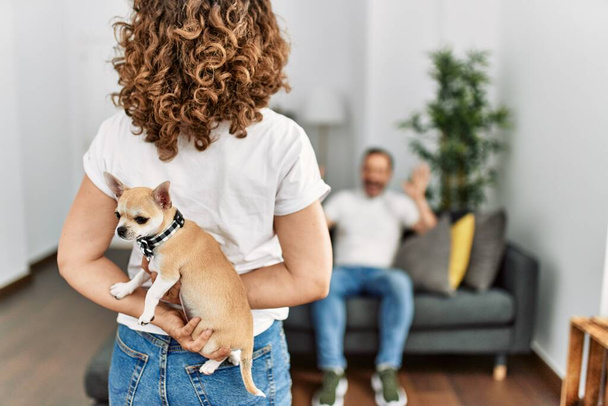 Mujer sorprendiendo a su marido con adorable perro en casa. - Foto, Imagen