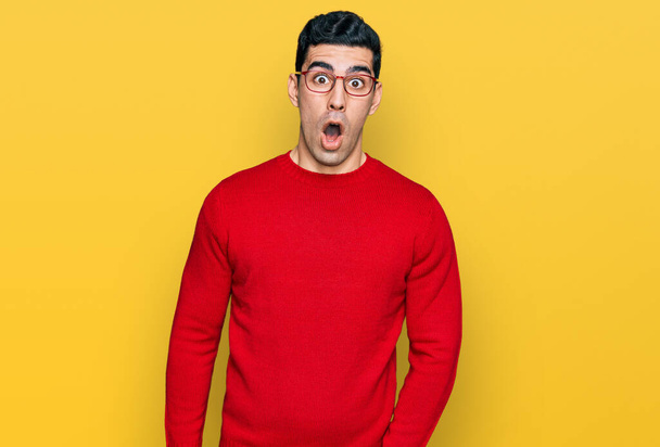 Hombre hispano guapo vistiendo ropa casual y gafas asustado y sorprendido con expresión sorpresa, miedo y cara excitada.  - Foto, imagen