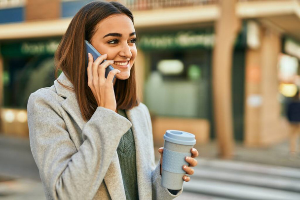 Jovencita hispana hablando en el smartphone tomando café en la ciudad. - Foto, imagen