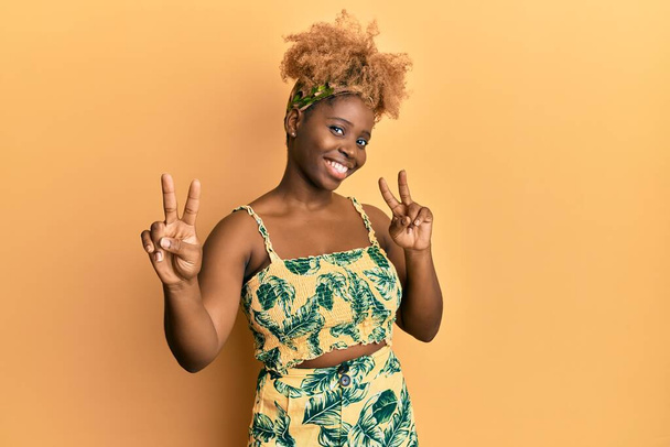 Young african woman with afro hair wearing summer dress smiling looking to the camera showing fingers doing victory sign. number two.  - Valokuva, kuva