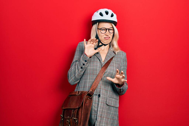 Beautiful caucasian blonde business woman wearing bike helmet disgusted expression, displeased and fearful doing disgust face because aversion reaction. with hands raised  - Foto, imagen