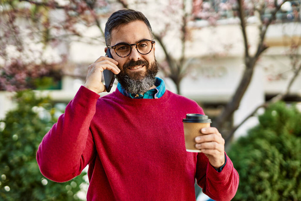Junger hispanischer Geschäftsmann spricht auf dem Smartphone und trinkt Kaffee in der Stadt. - Foto, Bild