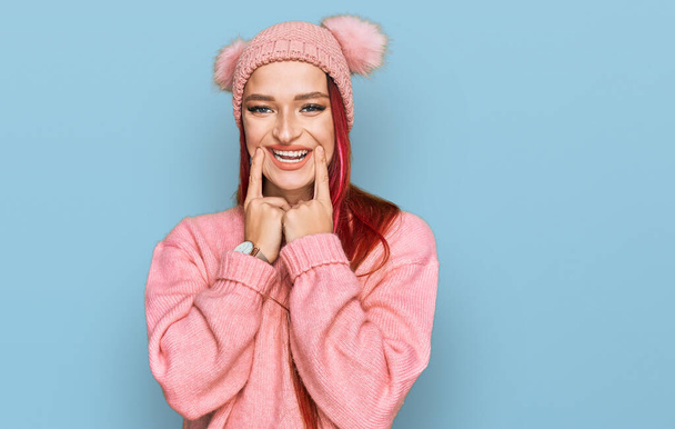 Νεαρή καυκάσια γυναίκα φορώντας casual ρούχα και μάλλινο καπέλο χαμογελώντας με ανοιχτό στόμα, δάχτυλα δείχνοντας και αναγκάζοντας χαρούμενο χαμόγελο  - Φωτογραφία, εικόνα