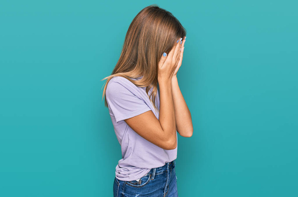 Teenager kaukasisches Mädchen in lässiger Kleidung mit traurigem Gesichtsausdruck, das Gesicht mit Händen bedeckt, während es weint. Depressionskonzept.  - Foto, Bild