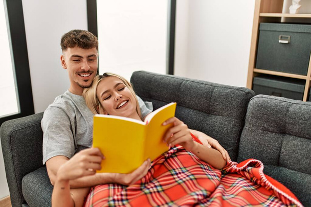 Junges kaukasisches Paar lächelt glücklich Buch zu Hause lesen. - Foto, Bild