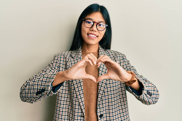Mulher chinesa jovem vestindo estilo de negócios e óculos sorrindo no amor fazendo forma de símbolo do coração com as mãos. conceito romântico.  - Foto, Imagem
