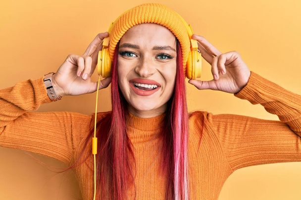若い白人女性がヘッドフォンを使用して音楽を聞いて笑顔で幸せとクールな笑顔で笑顔。歯を見せて.  - 写真・画像