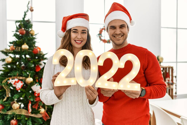 Jovem casal hispânico sorrindo feliz celebrar o ano novo segurando 2022 luzes em casa. - Foto, Imagem