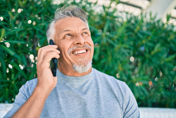 Middle age hispanic grey-haired man smiling happy talking on the smartphone at the park. - Photo, image