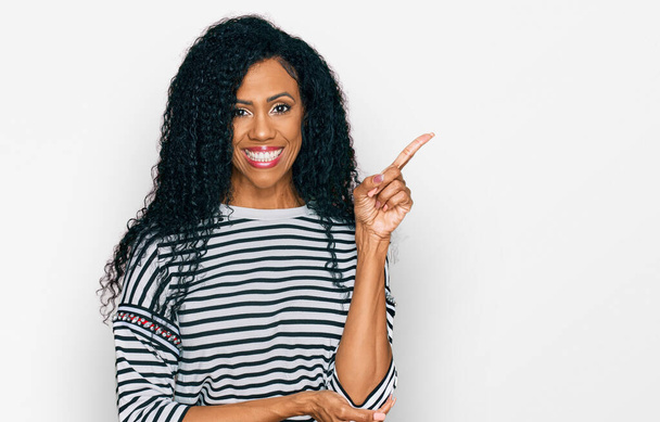 Középkorú afro-amerikai nő alkalmi ruhát visel egy nagy mosollyal az arcán, mutató kézzel és ujjal oldalra nézi a kamerát.  - Fotó, kép
