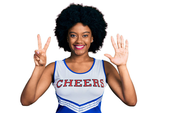 Nuori afrikkalainen amerikkalainen nainen yllään cheerleader univormu näyttää ja osoittaa sormilla numero seitsemän hymyillen itsevarma ja onnellinen.  - Valokuva, kuva