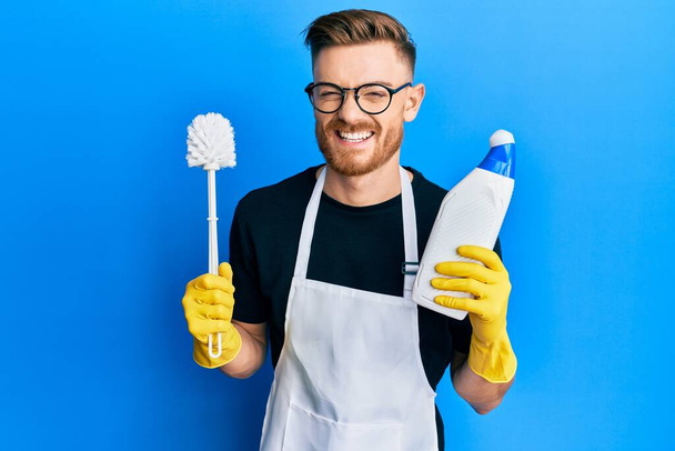 Junger rothaariger Mann macht Badezimmer-Hausarbeit mit Klobürste lächelnd und laut lachend, weil lustig verrückter Witz.  - Foto, Bild