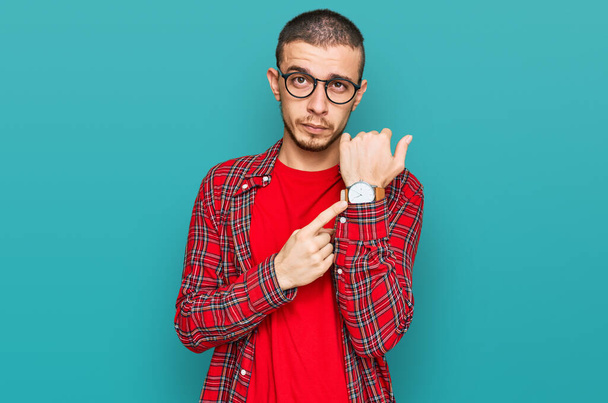 Hispanic young man wearing casual clothes in hurry pointing to watch time, impatience, looking at the camera with relaxed expression  - Photo, image