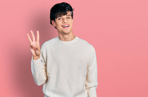 Knappe hipster jongeman draagt casual winter trui tonen en wijzen met vingers nummer drie, terwijl glimlachen zelfverzekerd en gelukkig.  - Foto, afbeelding