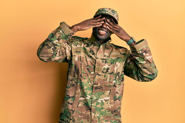 Young african american man wearing army uniform covering eyes with hands smiling cheerful and funny. blind concept.  - Foto, Bild