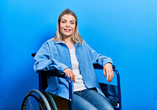Όμορφη καυκάσια γυναίκα κάθεται σε αναπηρική καρέκλα με ένα χαρούμενο και δροσερό χαμόγελο στο πρόσωπο. τυχερό άτομο.  - Φωτογραφία, εικόνα