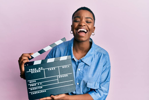 Genç Afro-Amerikalı kadın elinde video film panosu tutarak kahkahalarla gülüyor..  - Fotoğraf, Görsel