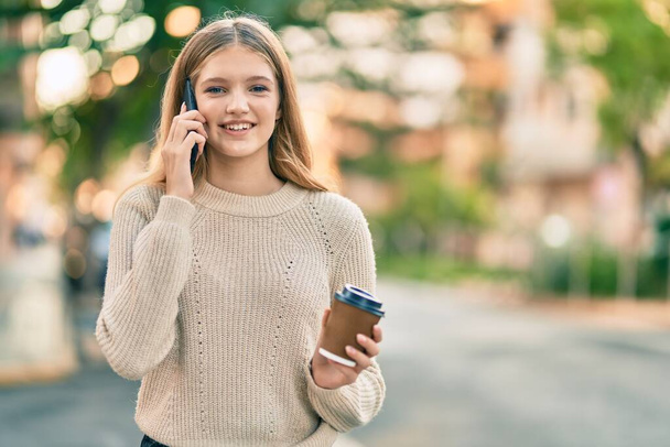 Όμορφη καυκάσιος έφηβος χαμογελά χαρούμενος μιλώντας στο smartphone στην πόλη. - Φωτογραφία, εικόνα