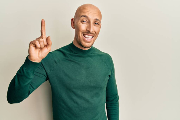 Bald man with beard wearing casual turtleneck sweater smiling with an idea or question pointing finger up with happy face, number one  - Photo, Image
