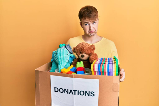 Young caucasian man holding donation box with toys depressed and worry for distress, crying angry and afraid. sad expression.  - Photo, Image