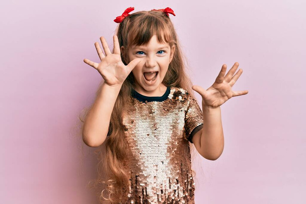 Little caucasian girl kid wearing festive sequins dress showing and pointing up with fingers number ten while smiling confident and happy.  - Photo, Image