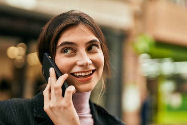 Νεαρή όμορφη επιχειρηματίας χαμογελώντας ευτυχισμένη μιλώντας στο smartphone στην πόλη. - Φωτογραφία, εικόνα