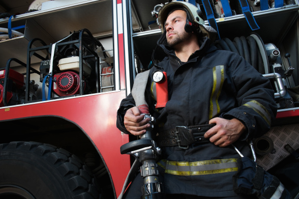 Feuerwehrmann nahe LKW mit Ausrüstung mit Wasserschlauch über Schulter  - Foto, Bild
