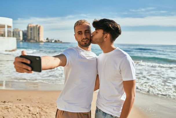 Genç eşcinsel çift kumsalda telefon başında mutlu bir şekilde selfie çekiyor.. - Fotoğraf, Görsel