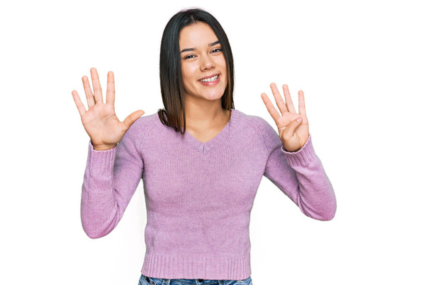 Fiatal spanyol lány hétköznapi ruhákat visel, kilences számú ujjakkal mutogat, miközben magabiztosan és boldogan mosolyog..  - Fotó, kép