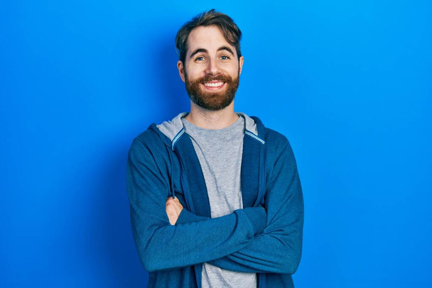 Caucasian man with beard wearing casual sweatshirt happy face smiling with crossed arms looking at the camera. positive person.  - Foto, Imagen