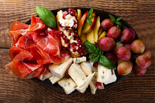  A set of appetizers for wine, jamon, pepperoni, cheese, grapes, peach on a plate top view. Snack board on wooden background, close up - Photo, image