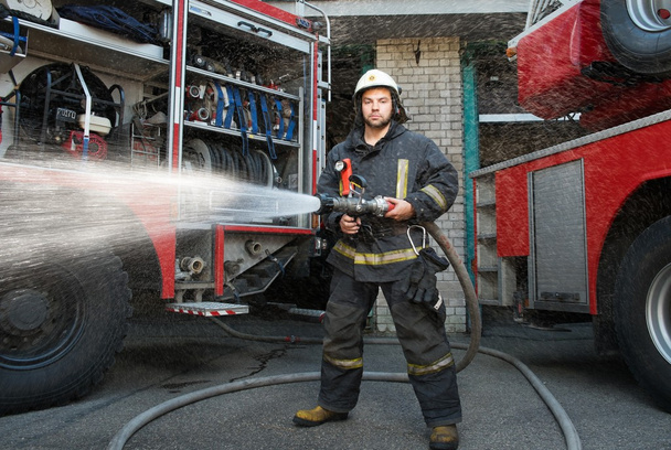 πυροσβέστης κρατώντας μάνικα νερού κοντά φορτηγό με εξοπλισμό  - Φωτογραφία, εικόνα