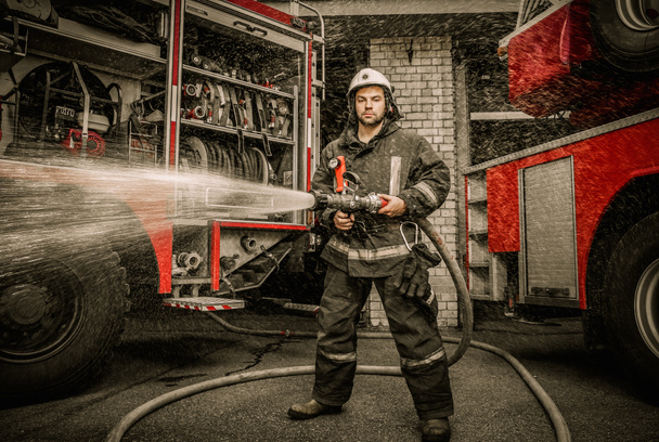 Пожарный держит водяной шланг возле грузовика с оборудованием
  - Фото, изображение