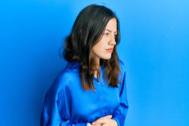 Giovane donna bruna indossa camicia blu casual con mano sullo stomaco perché indigestione, malattia dolorosa sensazione di malessere. concetto di dolore.  - Foto, immagini