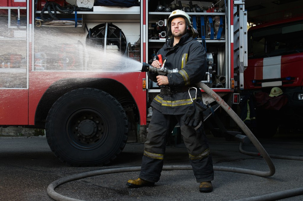 Pompier tenant tuyau d'eau près du camion avec de l'équipement
  - Photo, image