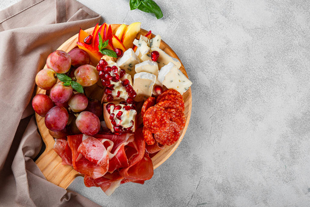  A set of appetizers for wine, jamon, pepperoni, cheese, grapes, peach on a wooden board top view. Snack board on light gray background, free space for text - Foto, imagen