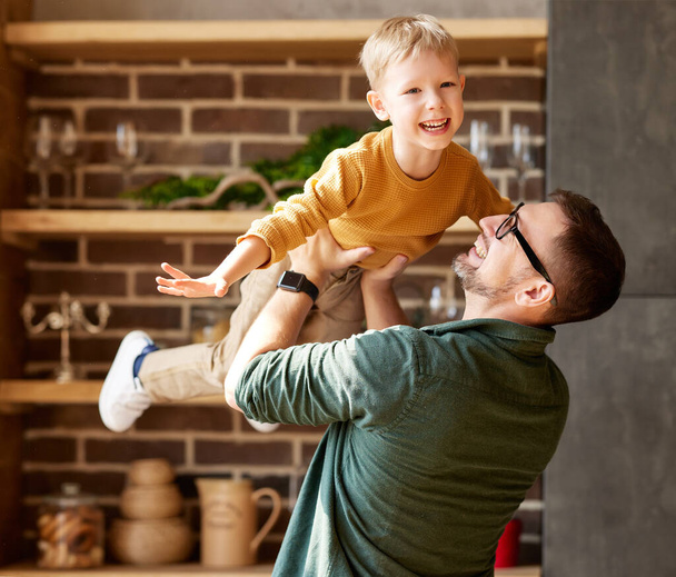 Playtime with dad. Little excited boy son flying in air in fathers arms while spending time together and having fun at home, young happy family daddy and child playing together indoors - Photo, Image
