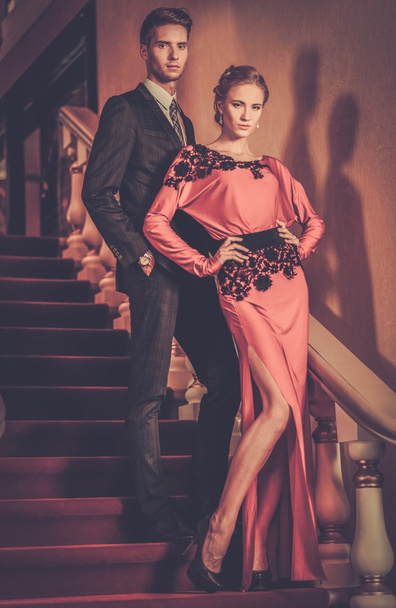 Beautiful well-dressed young couple standing on a steps in luxury interior  - Photo, Image