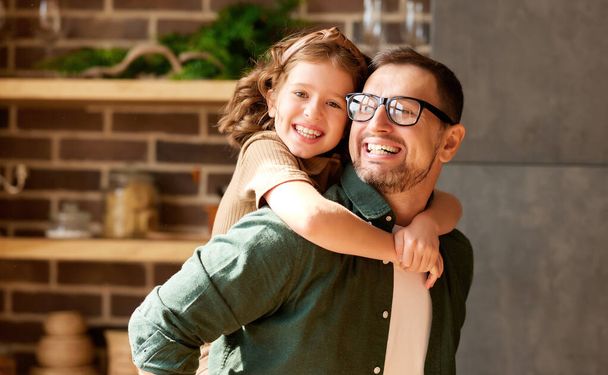 Best dad ever. Young loving father giving piggyback excited daughter, looking at her and smiling. Playful dad and adorable kid playing, having fun together at home. Family leisure activities concept - Photo, Image