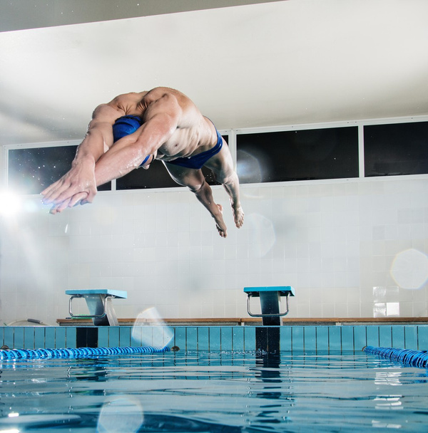 Joven nadador muscular saltando desde el bloque de partida en una piscina
 - Foto, Imagen
