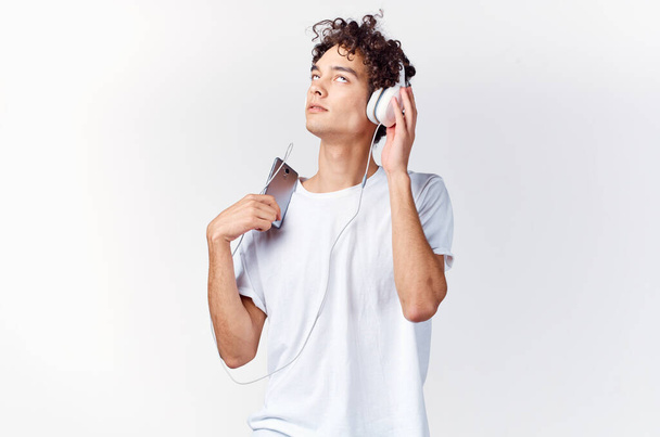 homme aux cheveux bouclés en t-shirt blanc écoutant de la musique avec casque technologie téléphone - Photo, image