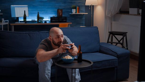 Конкурентоспособный мужчина играет в видеоигры в гостиной ночью - Фото, изображение