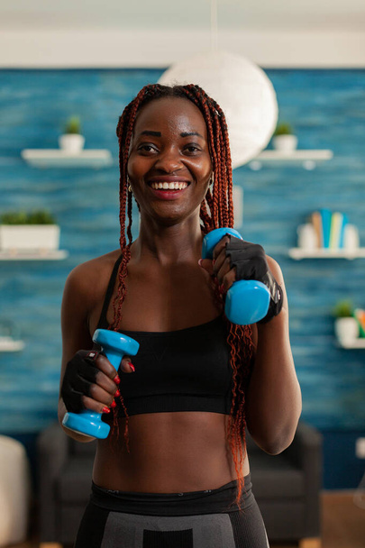 Přizpůsobit černošky žena cvičení biceps s činkami v obývacím pokoji - Fotografie, Obrázek