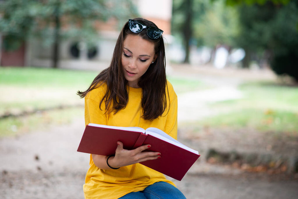 Young woman student writing on a book outdoor in a park - Foto, imagen